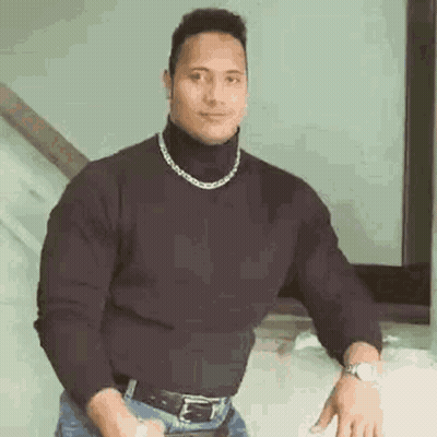 A Man Wearing A Black Turtleneck Sweater And A Chain Around His Neck Is Standing In Front Of A Mirror . GIF