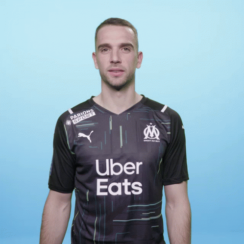 A Man Wearing A Black Uber Eats Shirt Stands In Front Of A Blue Background GIF