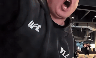 A Man Wearing A Black UFC Hoodie Is Screaming With His Mouth Open . GIF