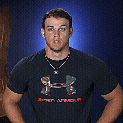 A Man Wearing A Black Under Armour Shirt Stands In Front Of A Blue Background GIF