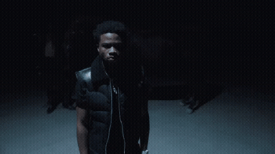 A Man Wearing A Black Vest And Headphones Stands In The Dark GIF