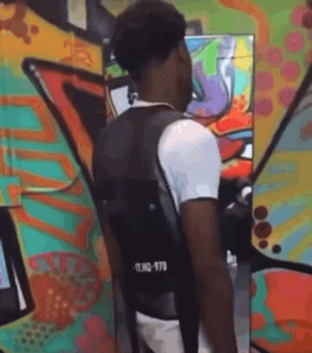 A Man Wearing A Black Vest Is Standing In Front Of A Colorful Graffiti Wall . GIF