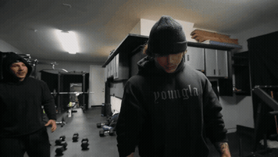 A Man Wearing A Black Youngla Hoodie Stands In A Gym GIF