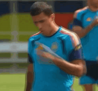 A Man Wearing A Blue Adidas Shirt Is Covering His Mouth With His Hand . GIF