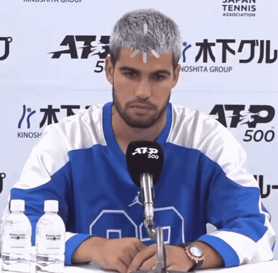 A Man Wearing A Blue And White Atp 500 Jersey Sits At A Table GIF