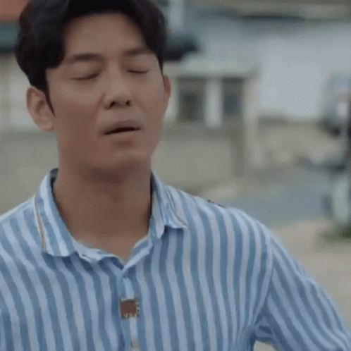 A Man Wearing A Blue And White Striped Shirt Is Holding His Hand To His Chest . GIF