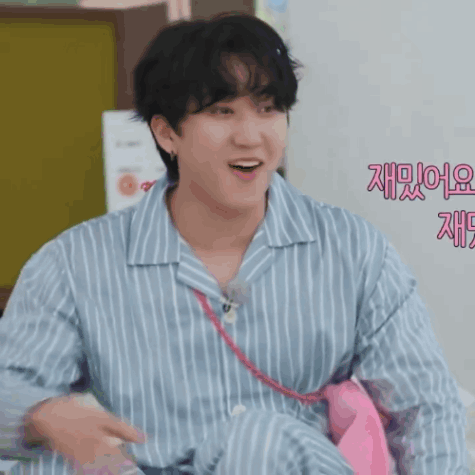 A Man Wearing A Blue And White Striped Shirt Is Smiling And Holding A Pink Tie GIF