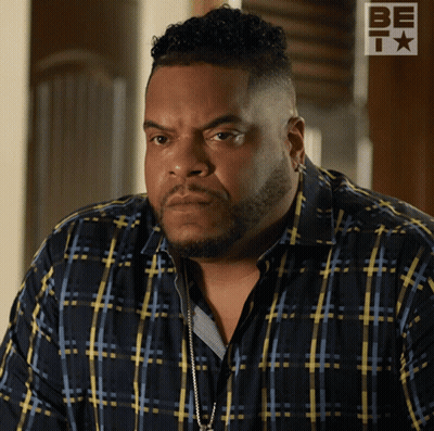 A Man Wearing A Blue And Yellow Plaid Shirt Is Standing In Front Of A Be T Logo GIF