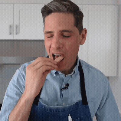 A Man Wearing A Blue Apron Eating A Piece Of Food GIF