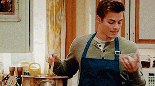 A Man Wearing A Blue Apron Is Cooking In A Kitchen . GIF