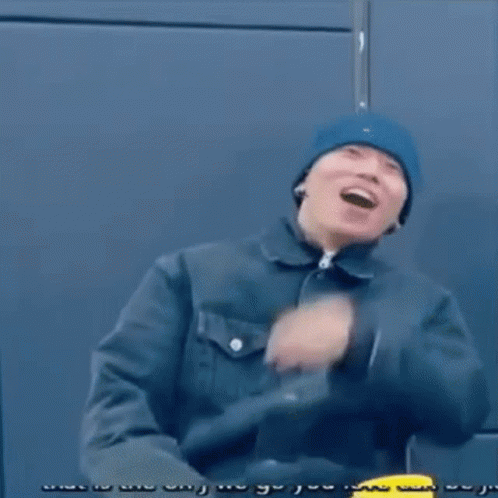 A Man Wearing A Blue Beanie And A Black Jacket Is Sitting On A Chair . GIF