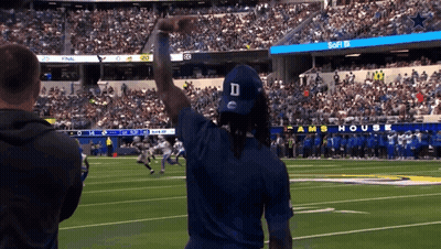 A Man Wearing A Blue D Hat Stands On A Football Field GIF