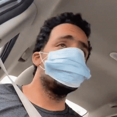 A Man Wearing A Blue Face Mask Is Sitting In A Car With A Seat Belt . GIF
