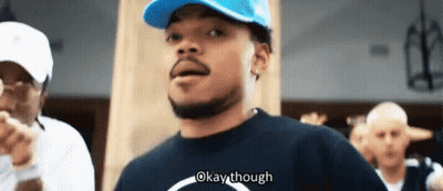 A Man Wearing A Blue Hat And A Black Shirt Is Standing In Front Of A Group Of People And Saying Okay Though . GIF