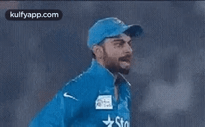A Man Wearing A Blue Hat And A Blue Jacket With A Star On It Is Walking On A Field . GIF