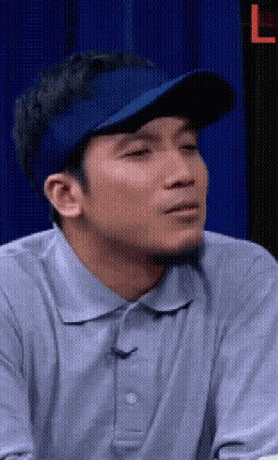 A Man Wearing A Blue Hat And A Grey Shirt Is Making A Face . GIF