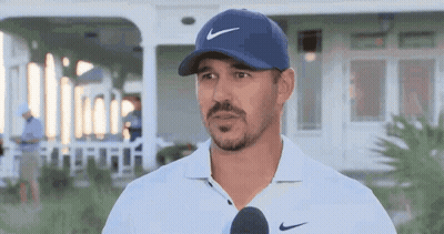 A Man Wearing A Blue Hat And A White Shirt Is Talking Into A Microphone . GIF