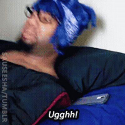 A Man Wearing A Blue Hat And Glasses Is Laying In A Sleeping Bag And Says Ugghh GIF