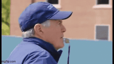 A Man Wearing A Blue Hat And Jacket Is Talking Into A Microphone . GIF