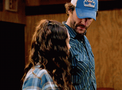 A Man Wearing A Blue Hat That Says Rancho Stands Next To A Woman GIF