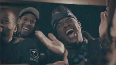 A Man Wearing A Blue Headband With The Letter G On It Is Laughing With Two Other Men . GIF