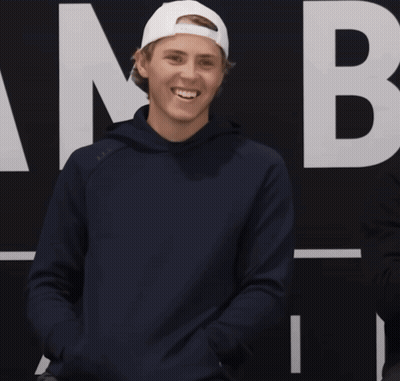 A Man Wearing A Blue Hoodie And A White Hat Is Smiling With A Question Mark In Front Of Him GIF