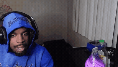 A Man Wearing A Blue Hoodie And Headphones Is Sitting In Front Of A Computer . GIF