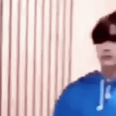 A Man Wearing A Blue Hoodie And Headphones Is Standing In Front Of A Window . GIF