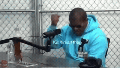 A Man Wearing A Blue Hoodie Is Sitting In Front Of A Microphone . GIF