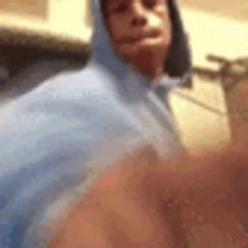 A Man Wearing A Blue Hoodie Is Taking A Selfie With His Phone . GIF