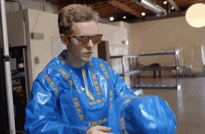 A Man Wearing A Blue Ikea Jacket And Sunglasses Holds A Blue Bag GIF