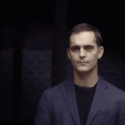 A Man Wearing A Blue Jacket And Black Shirt Is Smiling GIF