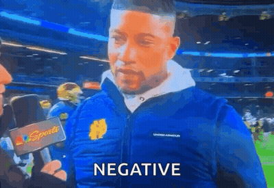 A Man Wearing A Blue Jacket Is Talking Into A Microphone And The Word Negative Is On The Screen . GIF