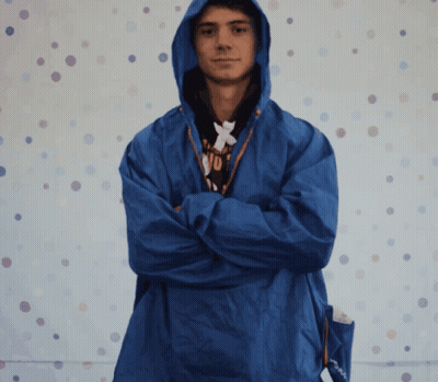 A Man Wearing A Blue Jacket With A Hood Has His Arms Crossed In Front Of A Polka Dot Background GIF