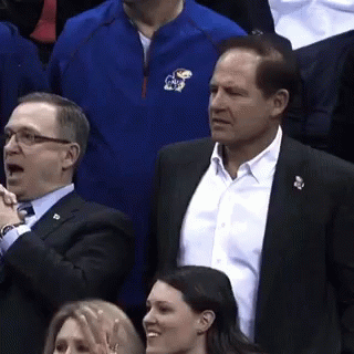 A Man Wearing A Blue Jacket With The Letter K On It Stands In A Crowd Of People GIF