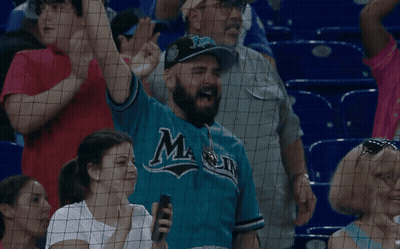 A Man Wearing A Blue Jersey With The Letter M On It Stands In A Crowd GIF