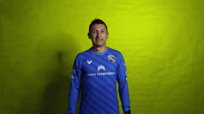 A Man Wearing A Blue Kaiser Permanent Jersey Stands In Front Of A Yellow Background GIF