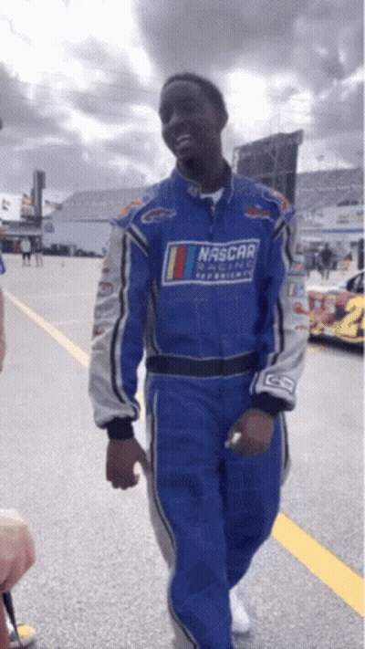 A Man Wearing A Blue Nascar Suit Walks Down A Road GIF