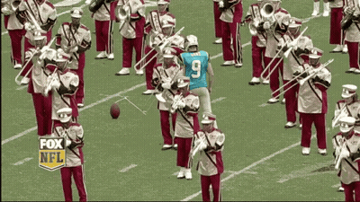 A Man Wearing A Blue Number 9 Jersey Stands In Front Of A Marching Band GIF