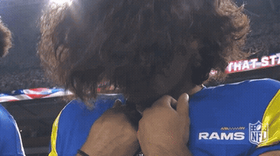 a man wearing a blue rams jersey covering his face with his hands