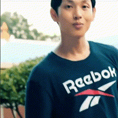 A Man Wearing A Blue Reebok Shirt Stands In Front Of Trees GIF