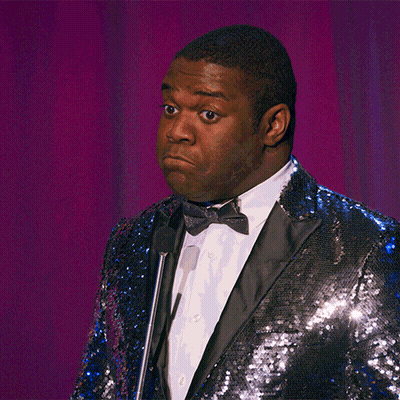 A Man Wearing A Blue Sequined Jacket And Bow Tie Stands In Front Of A Microphone GIF