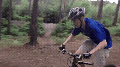 A Man Wearing A Blue Shirt And A Helmet Is Riding A Bike On A Dirt Road GIF