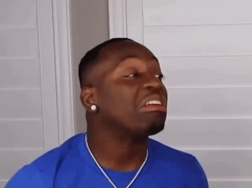 A Man Wearing A Blue Shirt And A Necklace Is Making A Face . GIF