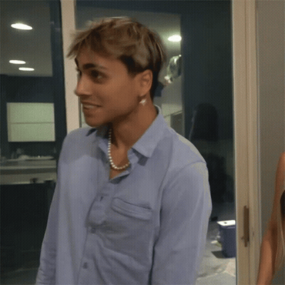 A Man Wearing A Blue Shirt And A Pearl Necklace Looks At The Camera GIF