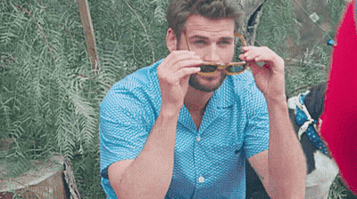 A Man Wearing A Blue Shirt And Sunglasses Is Sitting On A Chair . GIF