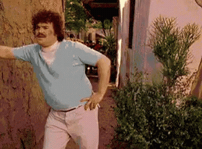 A Man Wearing A Blue Shirt And White Pants Is Standing In Front Of A Wall . GIF