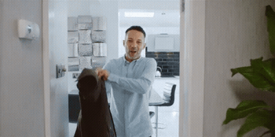 A Man Wearing A Blue Shirt Is Holding A Black Jacket GIF