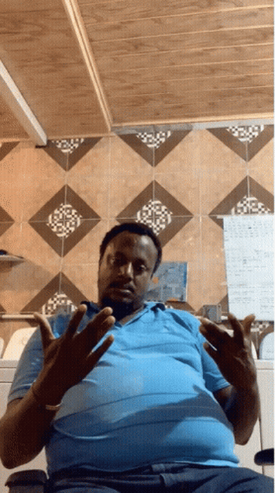 A Man Wearing A Blue Shirt Is Sitting In Front Of A Wall With A Calendar On It GIF