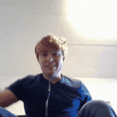 A Man Wearing A Blue Shirt Is Sitting On A Bed GIF